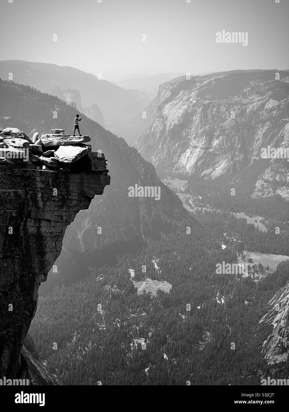 A male hiker taking a photo of the lower Yosemite Valley from the top of half dome. Yosemite National Park, California USA. - Smartphone Captured Stock Image