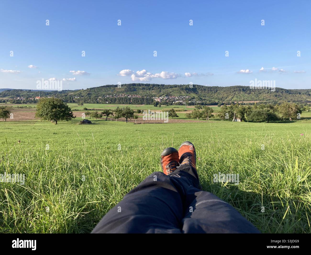 Legs and feet of hiker taking a break on a meadow in idyllic rural landscape in Southern Germany - Smartphone Captured Stock Image