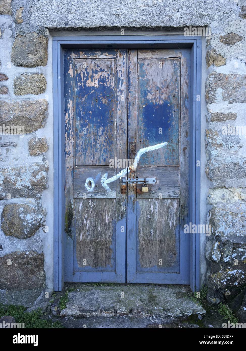 A weathered blue door with an arrow painted in white pointing to a key hole - Smartphone Captured Stock Image