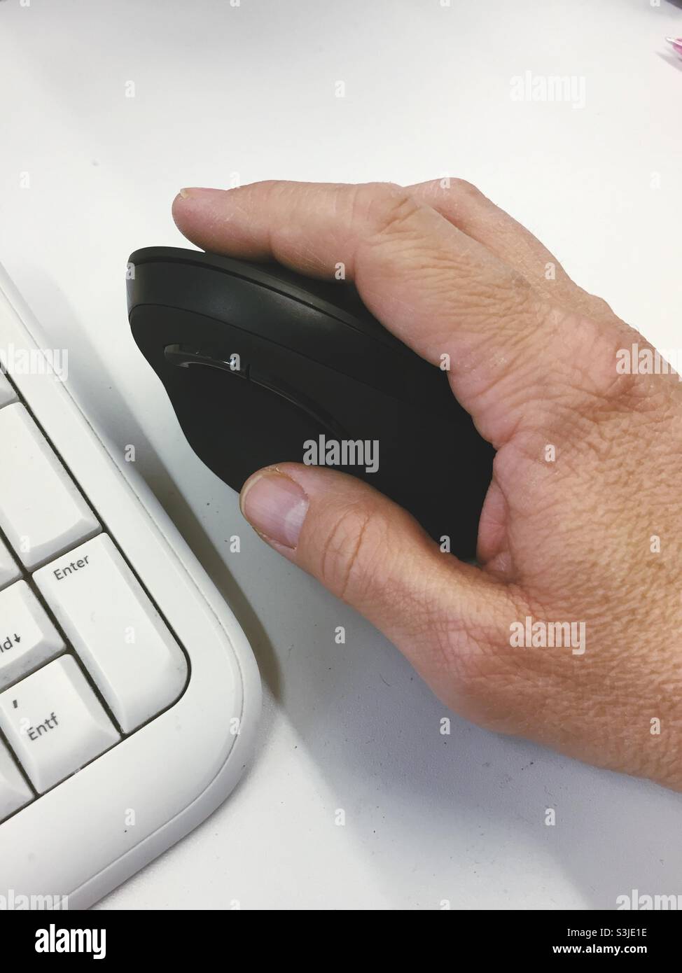 Hand with ergonomic computer mouse on a table near a keyboard - Smartphone Captured Stock Image