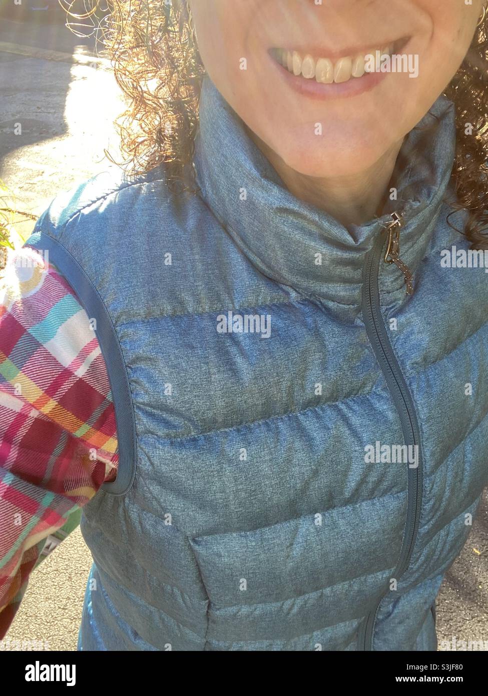 Smiling portrait of a woman wearing a plaid shirt and a down vest. - Smartphone Captured Stock Image
