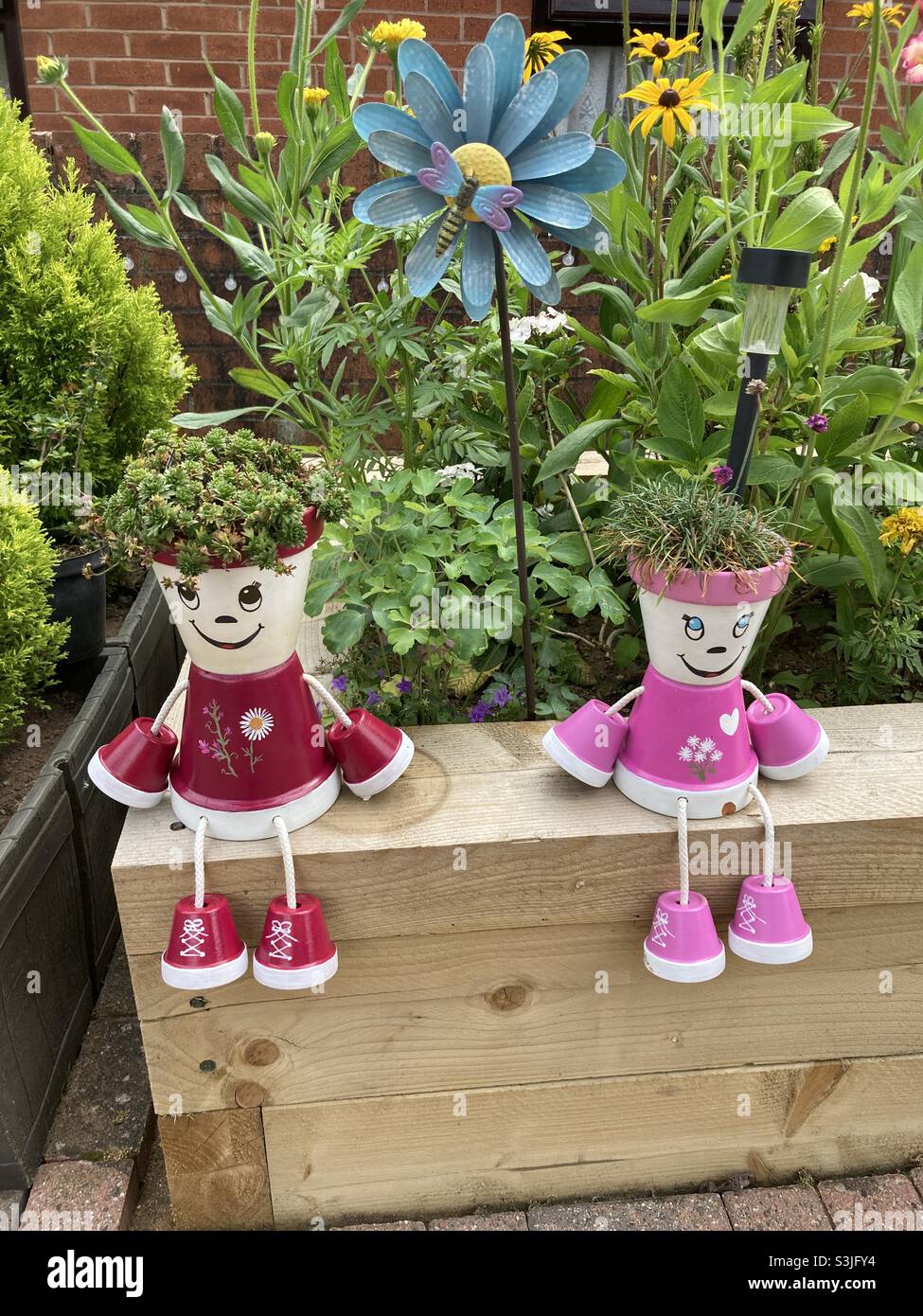 Flower pots made into people in the garden sitting on raised flower beds  made from railway sleepers Stock Photo - Alamy