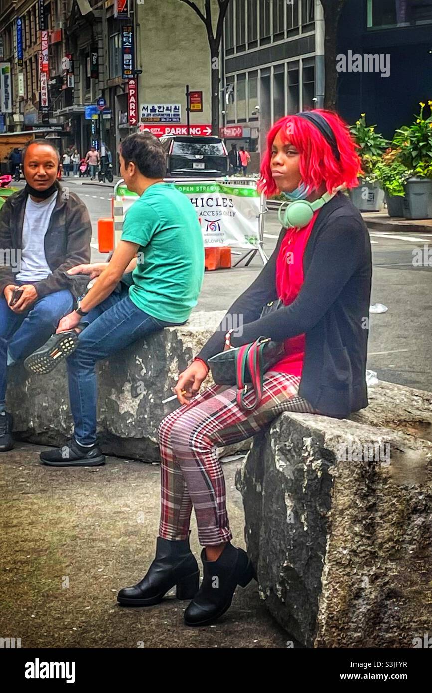 Black woman in red wig sitting on a rock smoking - Smartphone Captured Stock Image