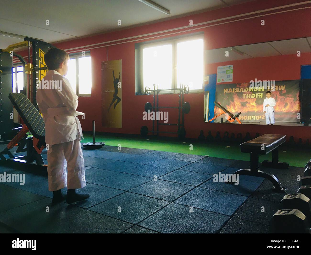 Boy child dressed for Judo stands in front of large mirror in gym, Hungary - Smartphone Captured Stock Image