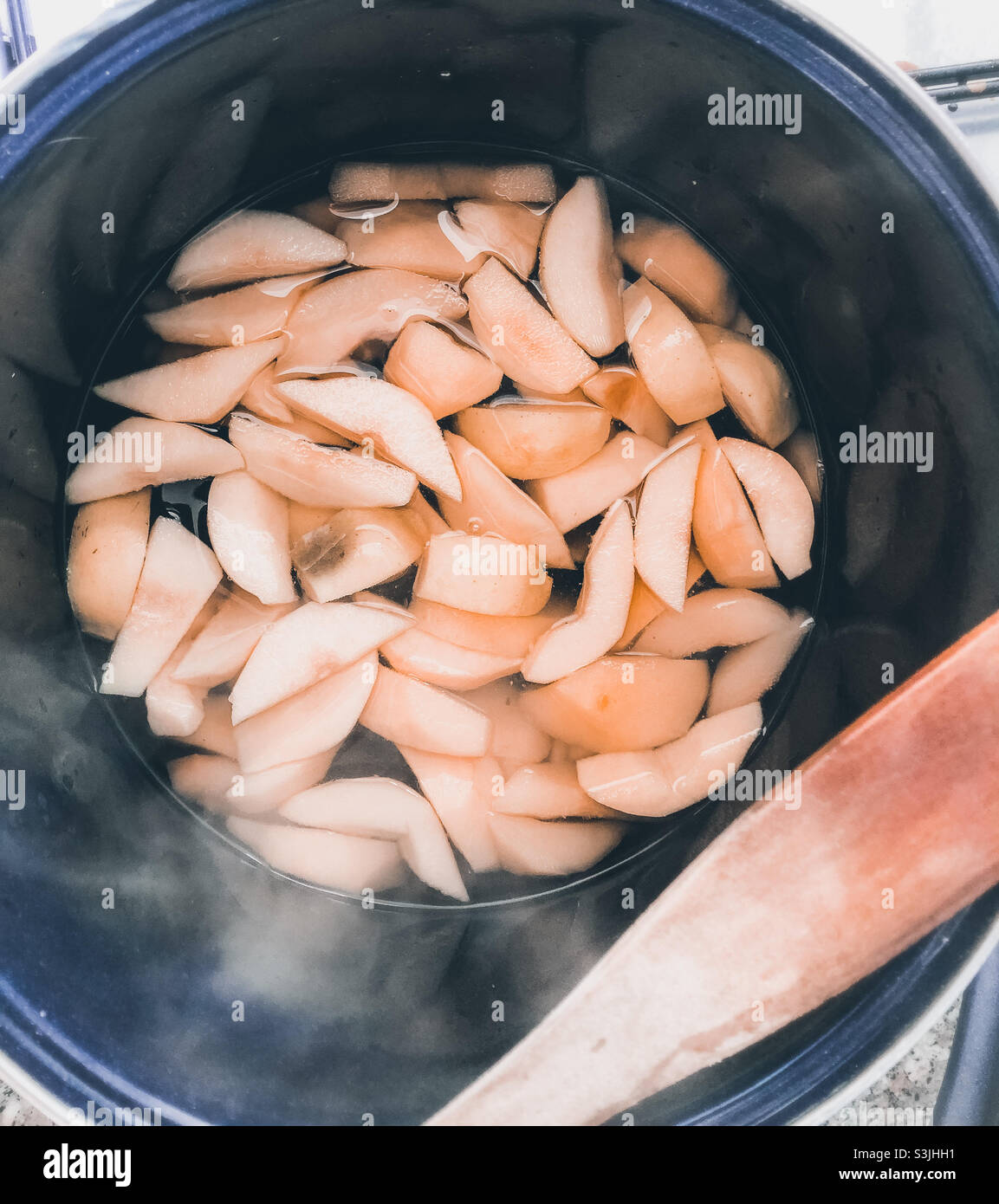 A shot looking down into a large pot of sliced quince steaming on the stove, with wooden spoon on one side - Smartphone Captured Stock Image