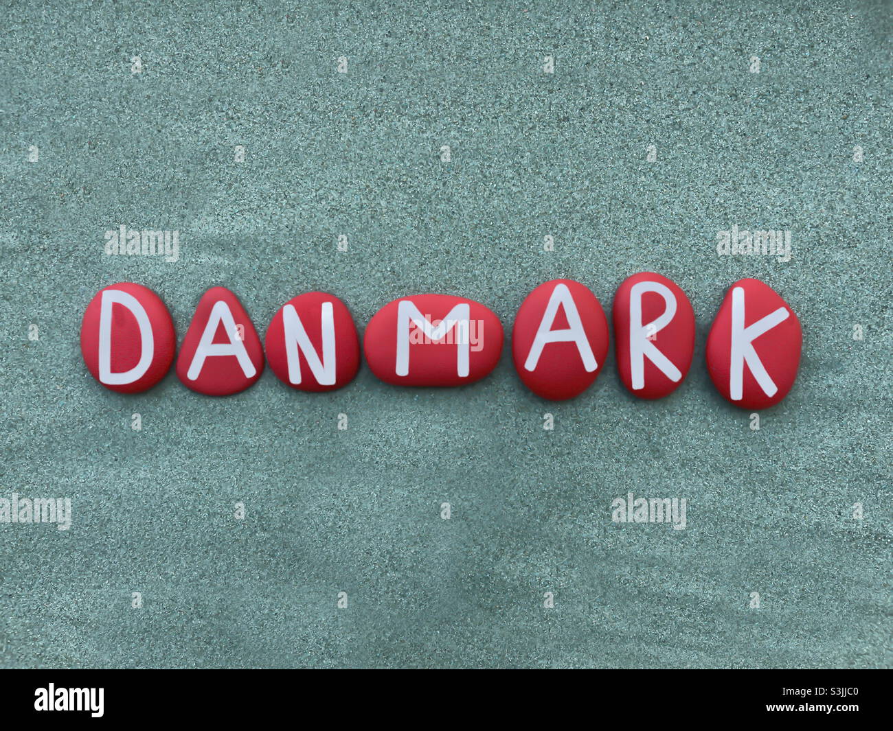 Danmark, Danish country name composed with red colored stone letters over green sand - Smartphone Captured Stock Image
