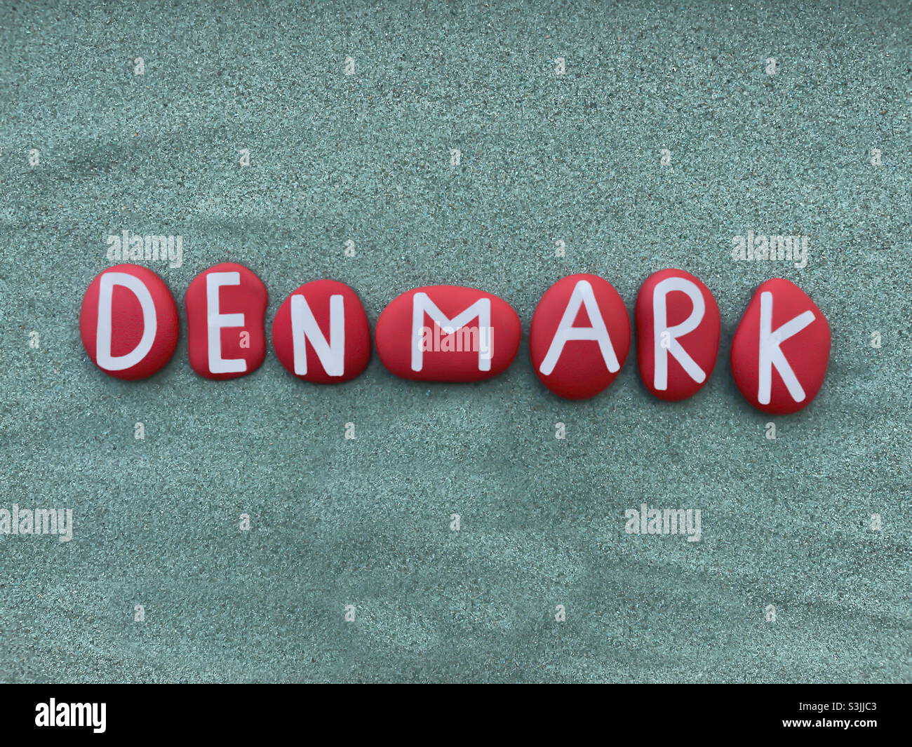 Denmark, country name composed with red colored stone letters over green sand - Smartphone Captured Stock Image