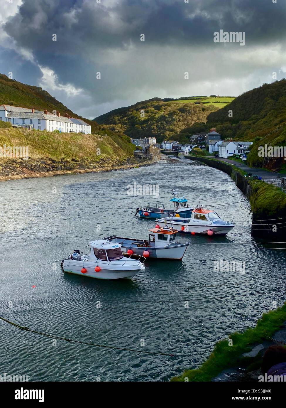 a line of fishing boats moored at the mouth of Boscastle harbour, Cornwall, England with ancient cittages on the hills - Smartphone Captured Stock Image
