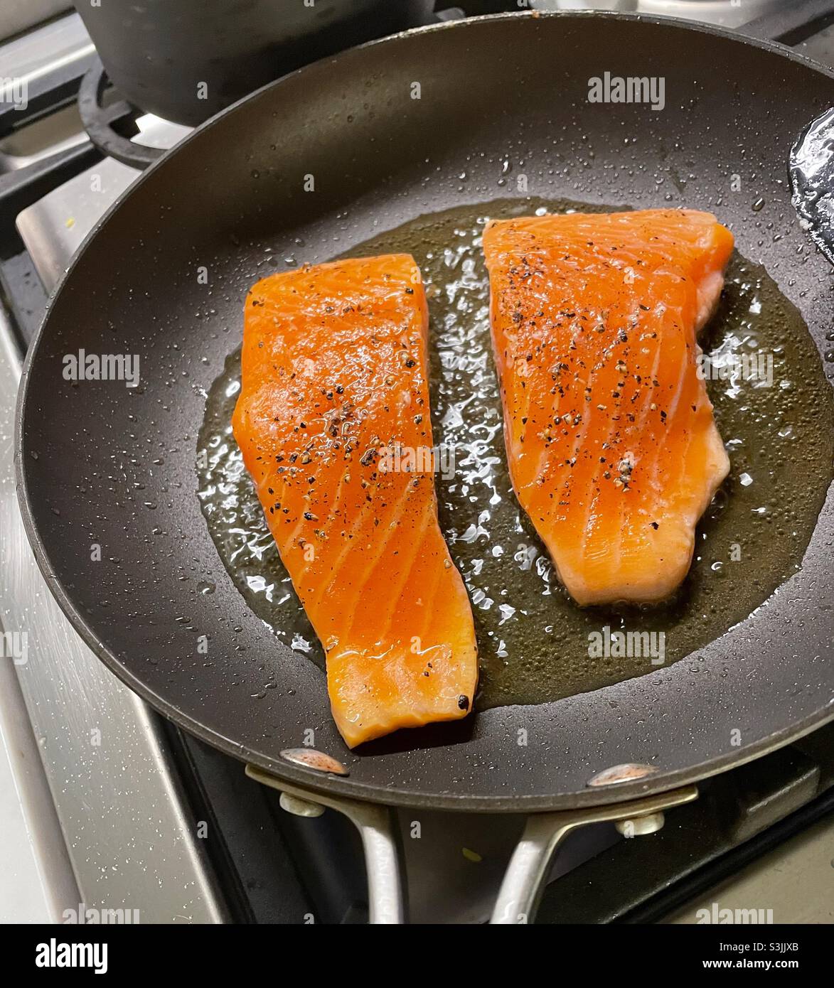 Close up of salmon fillets being sautéed in a skillet on a residential stove top, USA - Smartphone Captured Stock Image