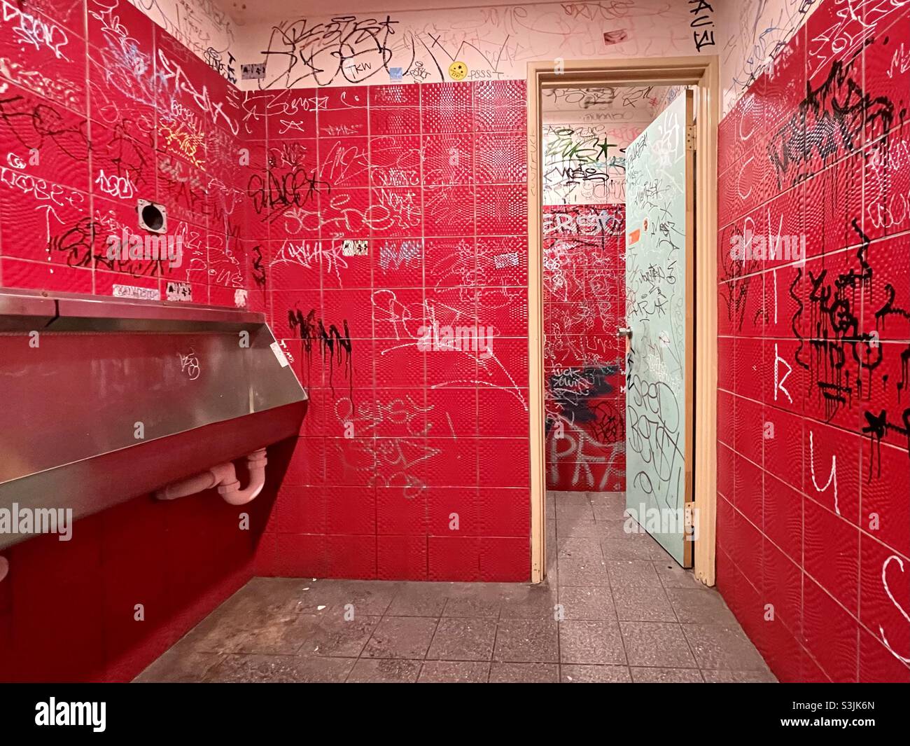 Urinal and graffiti on a red tiled male toilet Stock Photo