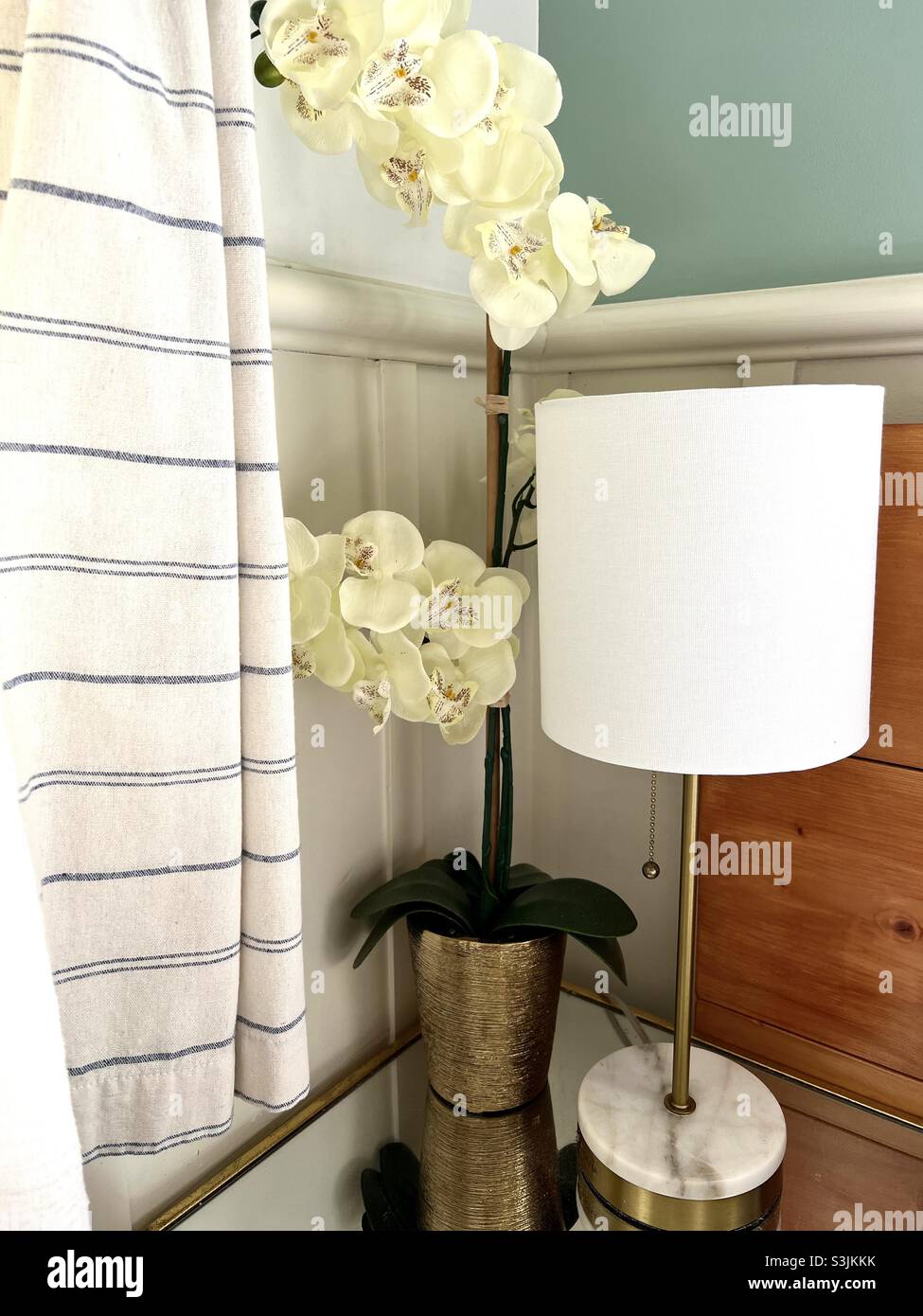 Gold marble lamp sits on mirrored nightstand next to Beautiful orchid. Stock Photo