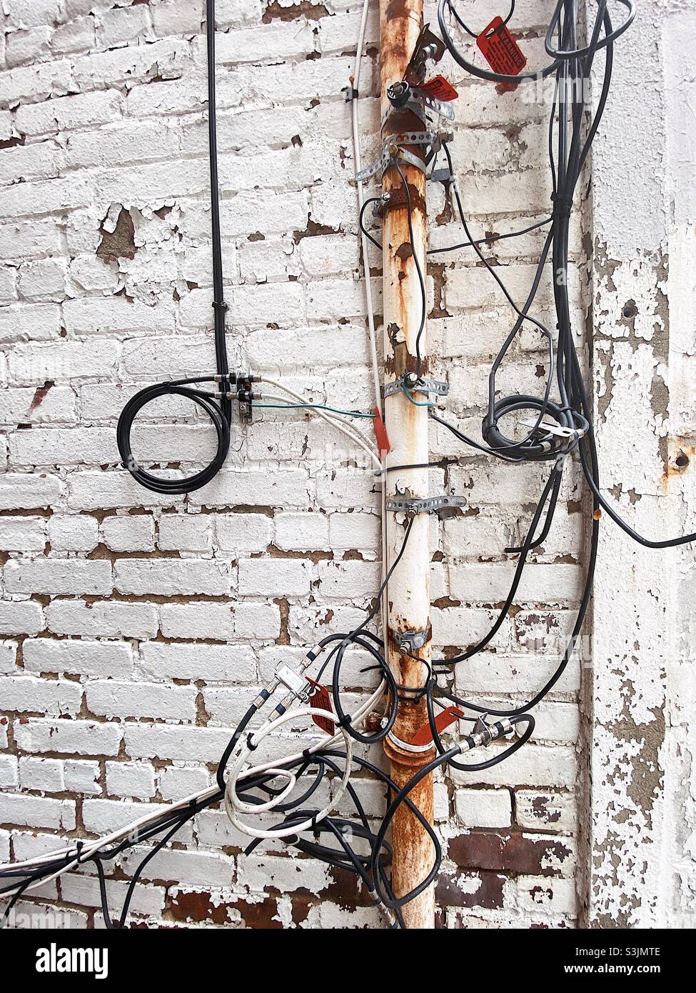 Tangled electrical wires and pipes in an old white exterior wall Stock Photo