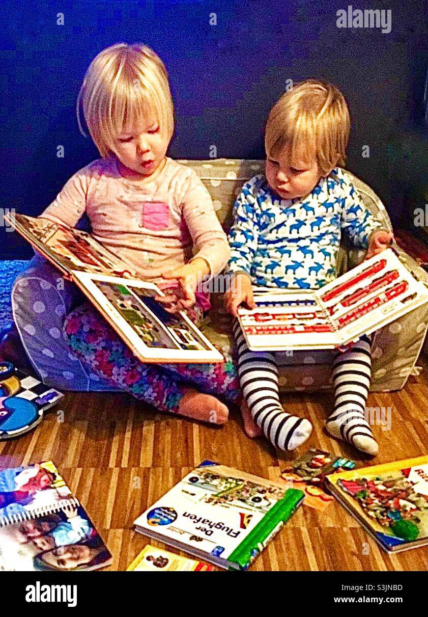 To blonde toddlers sitting in a child size sofa reading books - Smartphone Captured Stock Image