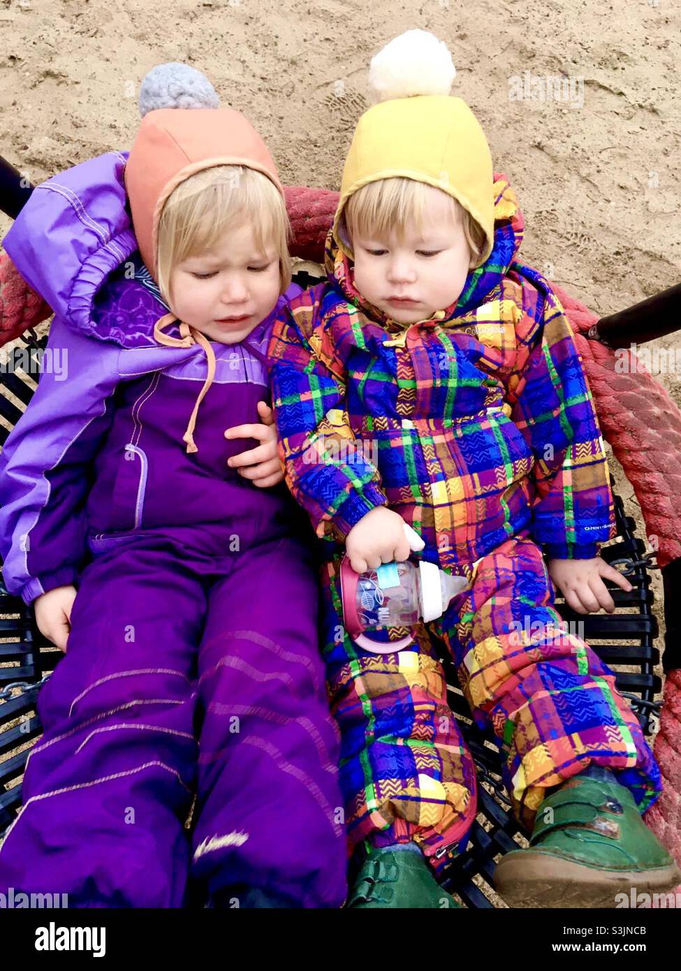 Two blonde toddlers in Brightly colored snow suits and knit hats - Smartphone Captured Stock Image