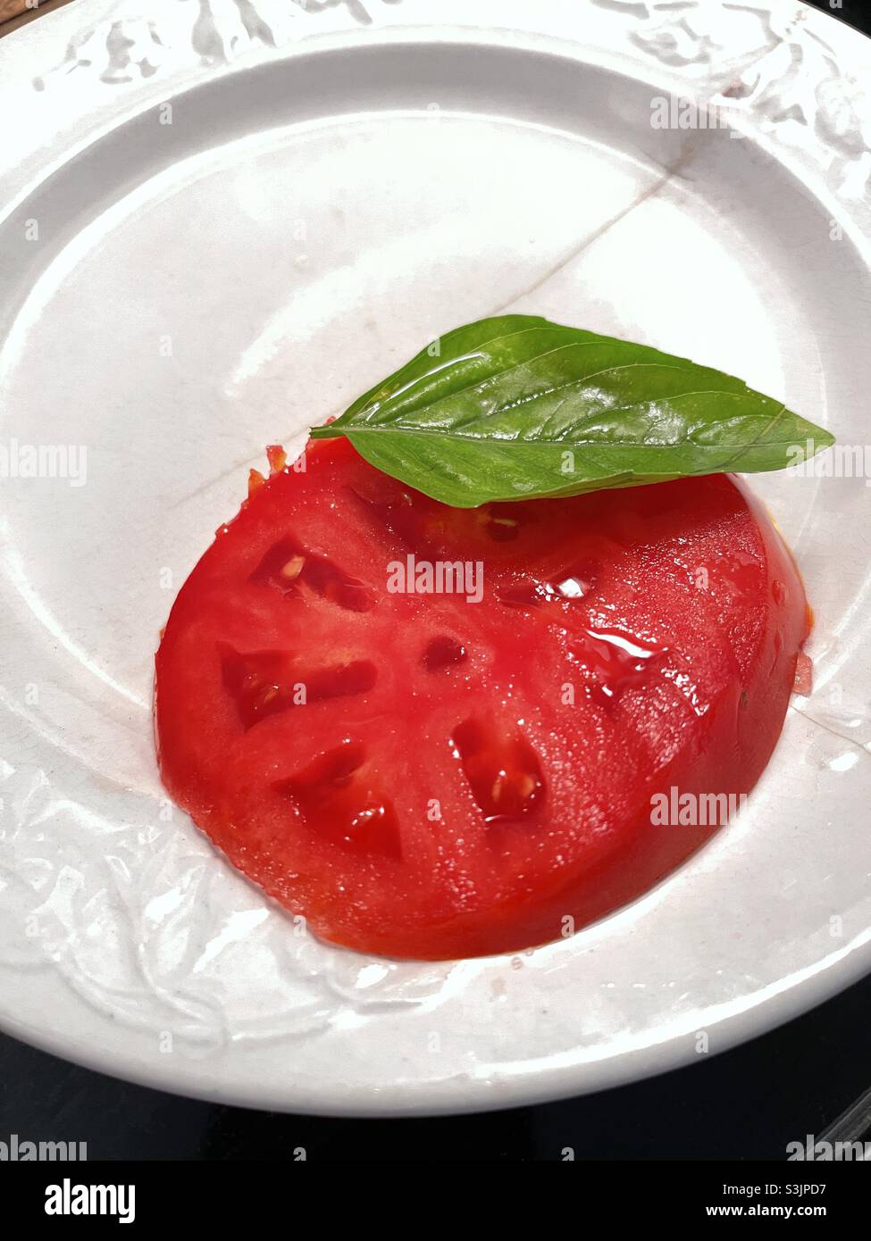 Tomato on plate with basil leaf Stock Photo