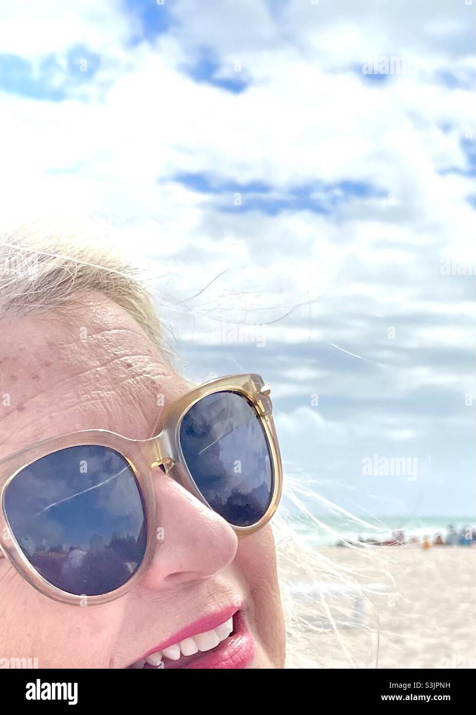 Partial close-up of a woman smiling in sunglasses at the beach - Smartphone Captured Stock Image