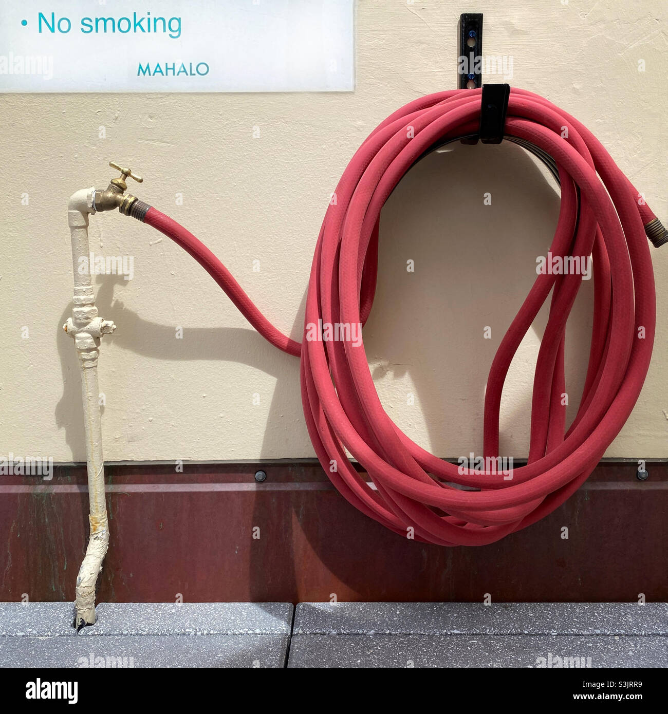 No smoking mahalo (thank you in Hawaiian) sign next to a red hose - Smartphone Captured Stock Image