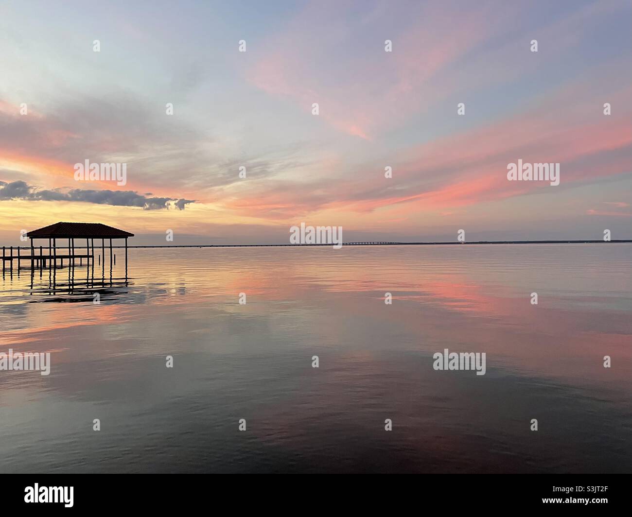 Colorful pastel sunset skies setting over calm bay water with boat dock ...