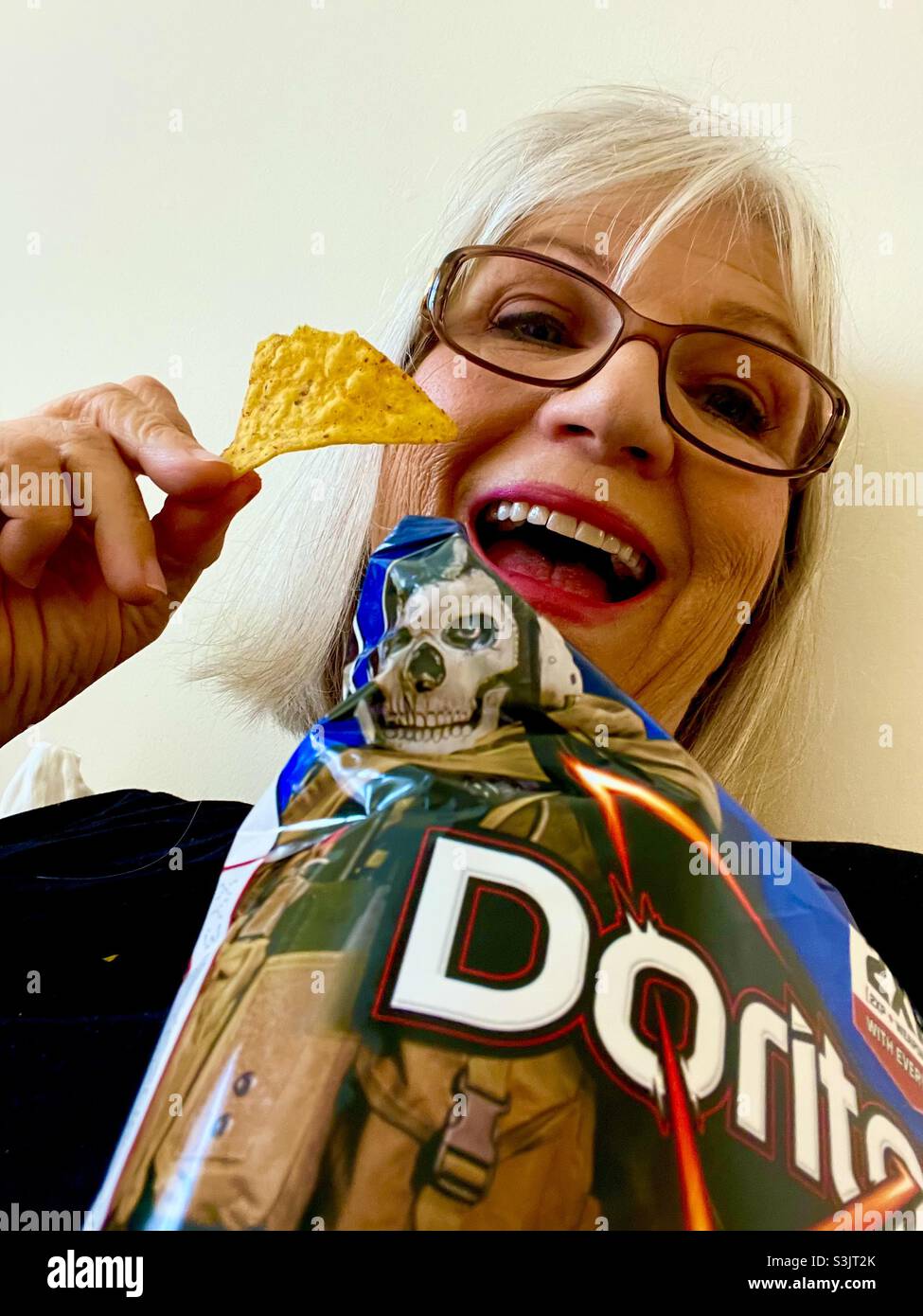 Woman laughing as she enjoys. Doritos chips - Smartphone Captured Stock Image