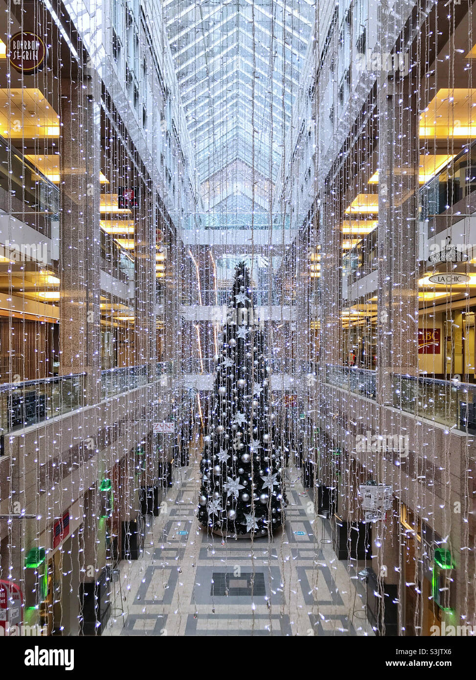 Looking through hanging Christmas lights towards the huge Christmas tree, decorated in silver ornaments. Bankers Hall, downtown Calgary, Alberta, Canada. - Smartphone Captured Stock Image