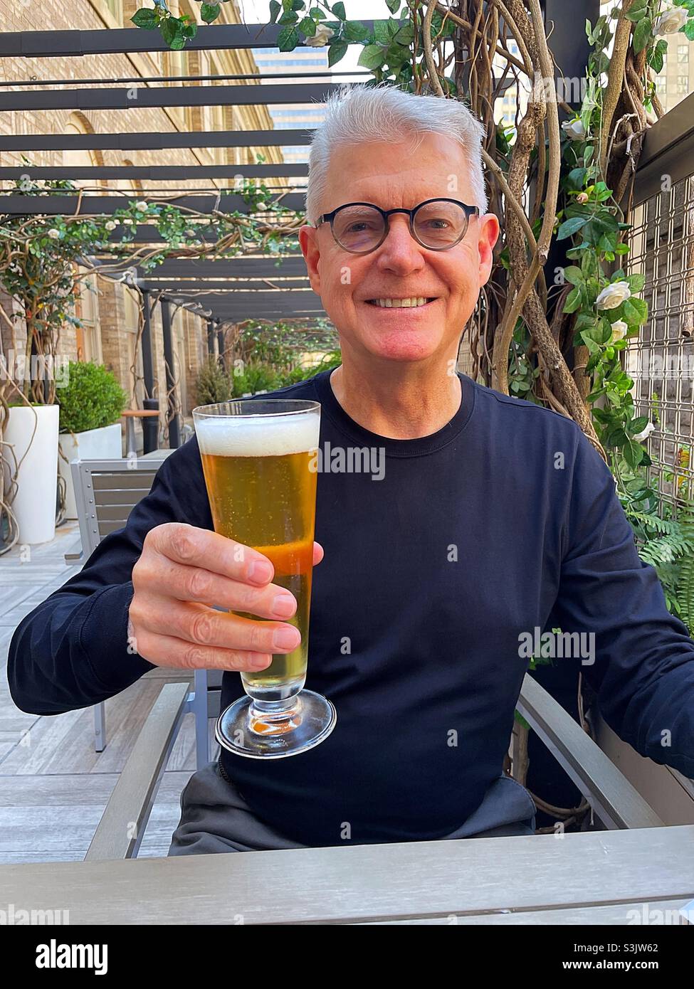 Senior man toasting a Pilsner glass of beer at an outdoor restaurant, NYC, USA, 2021 - Smartphone Captured Stock Image