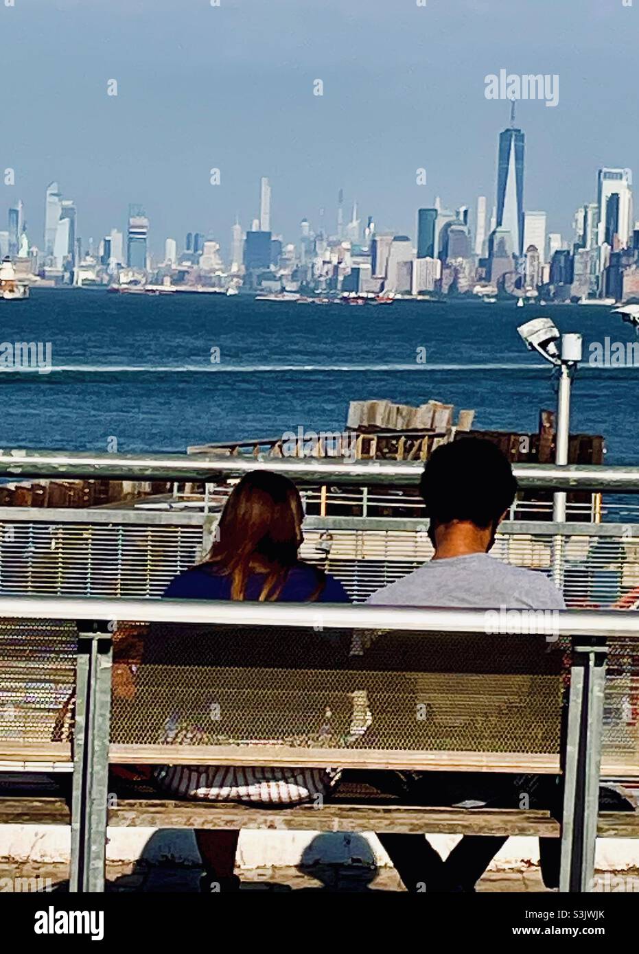 A couple sitting on a bench on Staten Island looking at the view of Manhattan - Smartphone Captured Stock Image