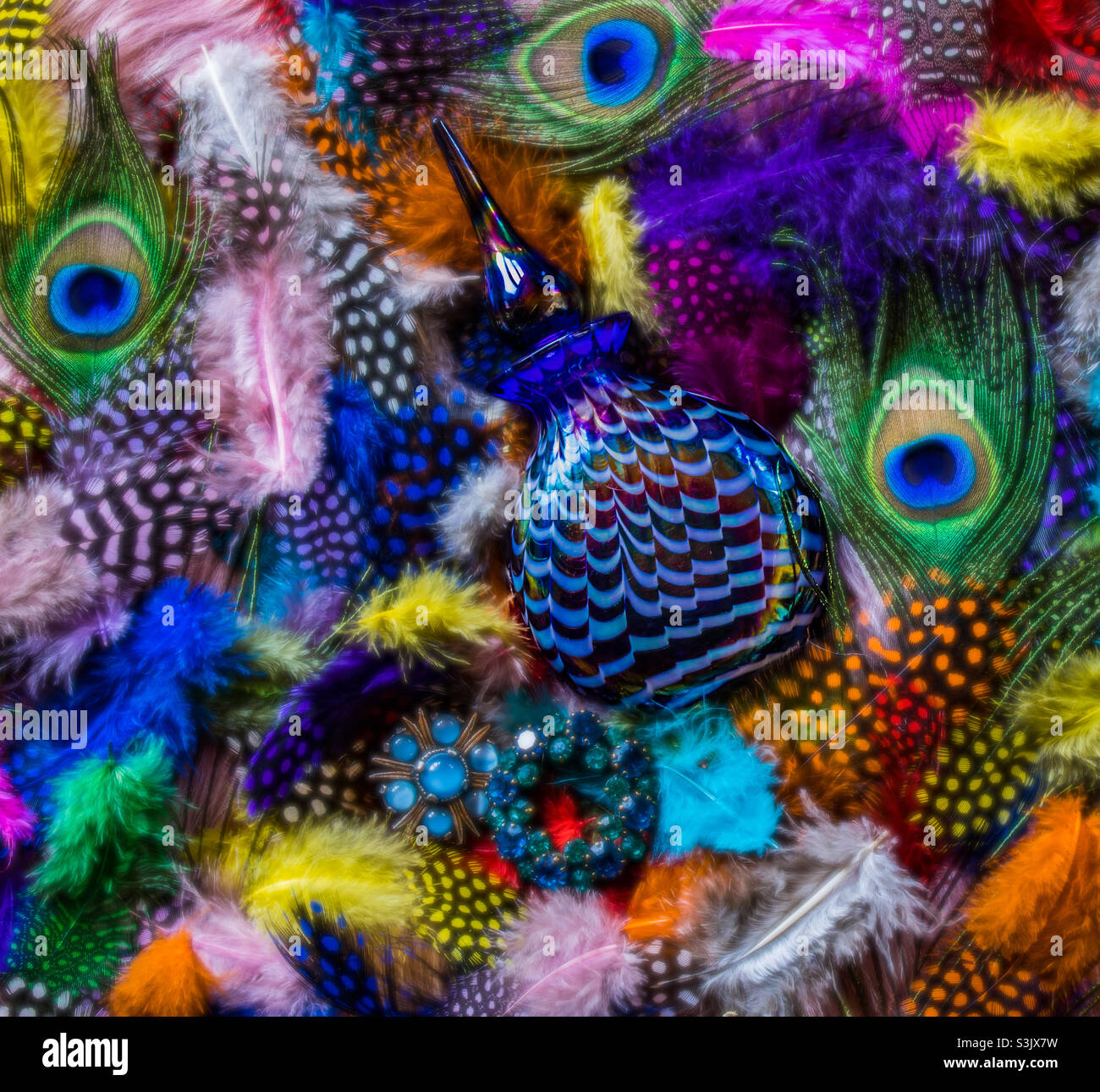 A blue, iridescent, Egyptian style lays on a bed of brightly coloured flowers alongside 2 blue brooches - Smartphone Captured Stock Image