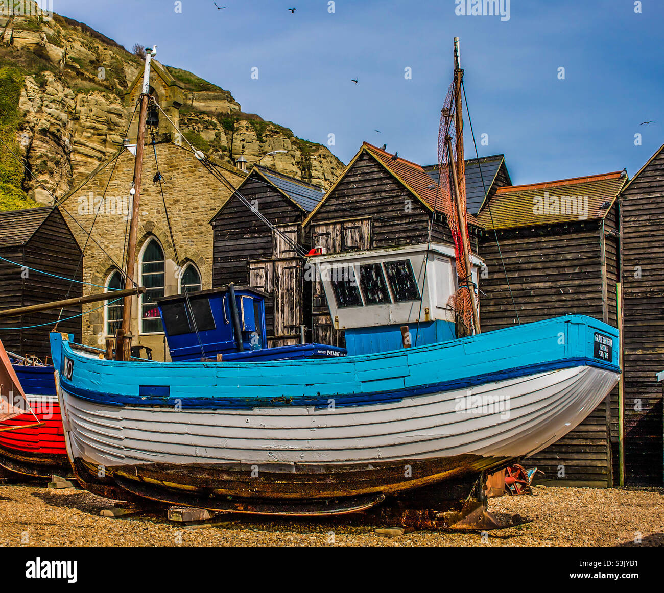 The blue and white Grace Georgina fishing vessel in front of the fishing huts and Fisherman’s museum in the Old Town of Hastings UK - Smartphone Captured Stock Image