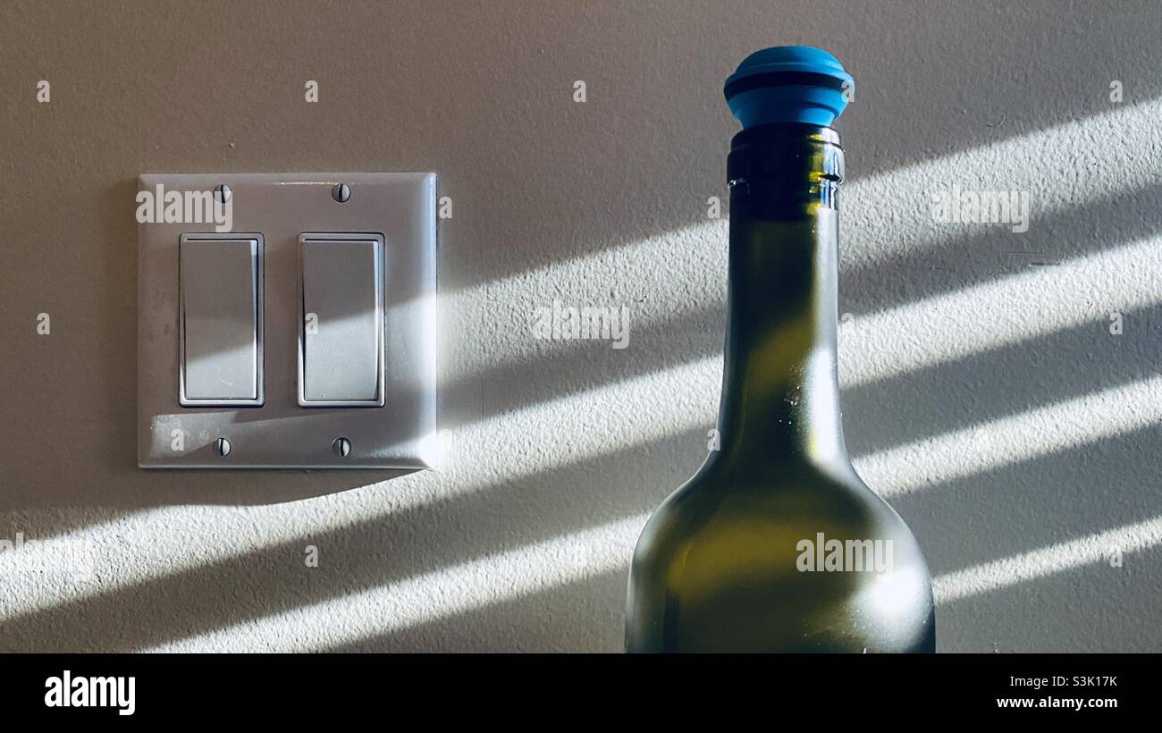 Top of green wine bottle with rubber stopper, white wall with shadow of venetian blinds, light switch - Smartphone Captured Stock Image