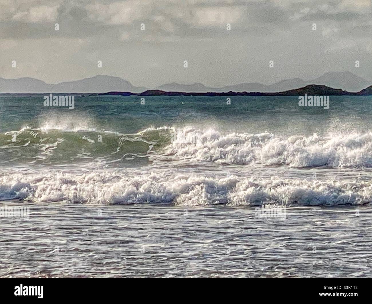 Crashing waves in beautiful October morning ligjt on traeth Cymyran, Rhosneigr, Valley, Anglesey, North Wales, Gwynedd, UK, view across to Snowdonia - Smartphone Captured Stock Image