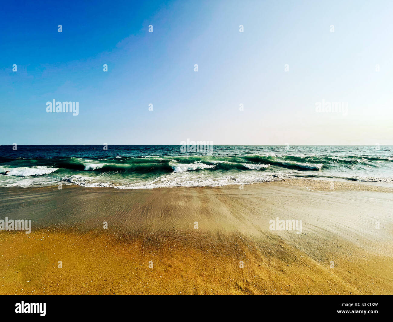 Ocean waves washing up onto sandy beach on a clear sunny day. - Smartphone Captured Stock Image