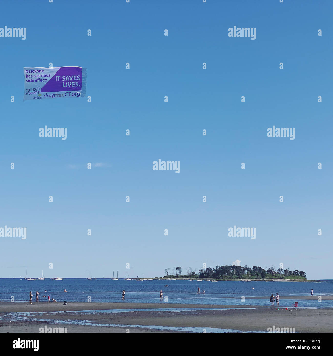 Sky banner advertising naloxone, a drug that prevents death from opioid overdose, flying over Silver Sands Beach, Silver Sands State Park, Milford, New Haven County,  Connecticut, United States - Smartphone Captured Stock Image