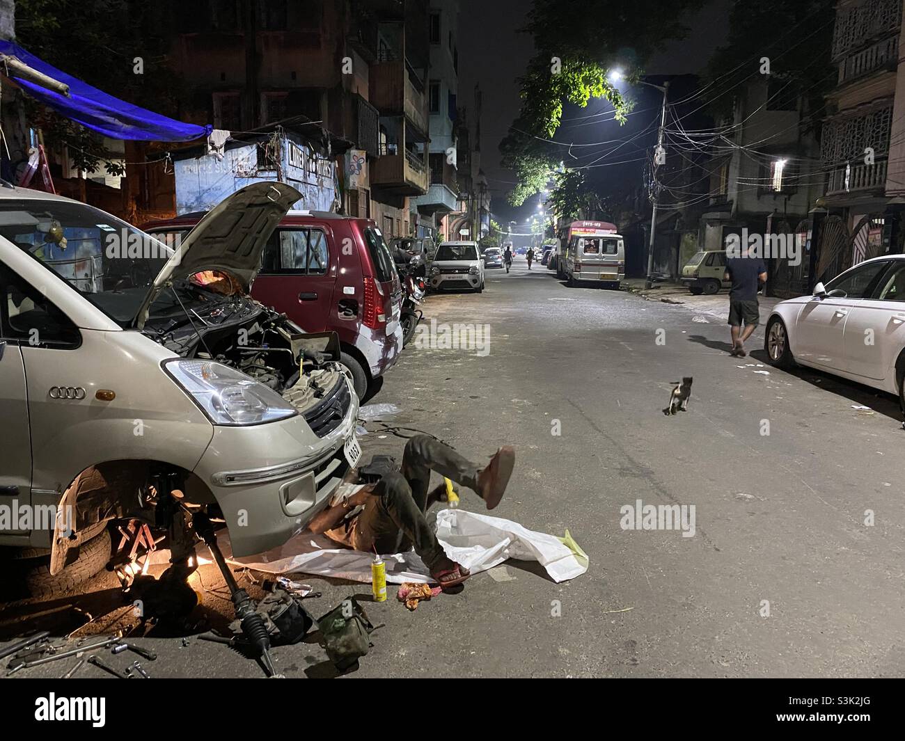 A mechanic repairing car lying on ground on a street at night - Smartphone Captured Stock Image
