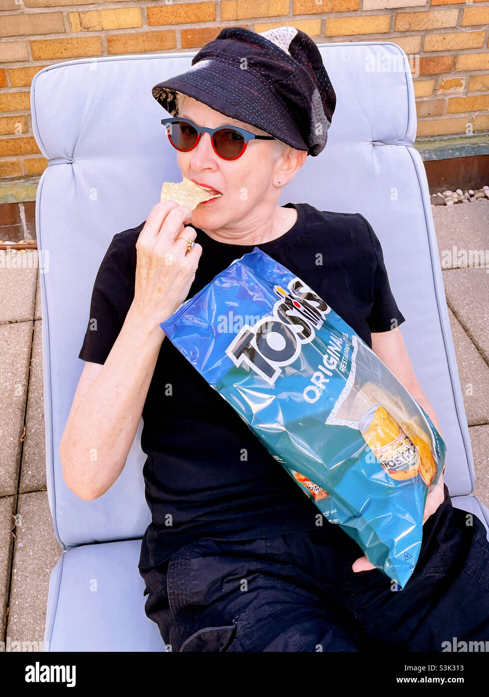 Senior woman lounging in an outdoor recliner eating Tostitos, 2021, USA - Smartphone Captured Stock Image