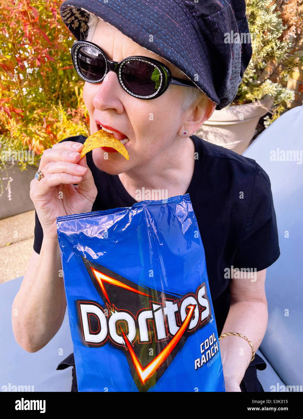 Well-dressed senior woman enjoying Doritos on a rooftop garden, USA, 2021 - Smartphone Captured Stock Image