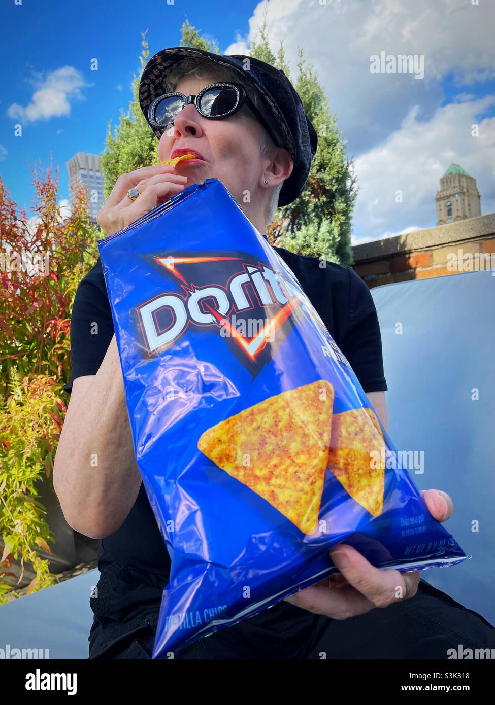 Senior woman sitting outside eating Doritos, 2021, USA - Smartphone Captured Stock Image