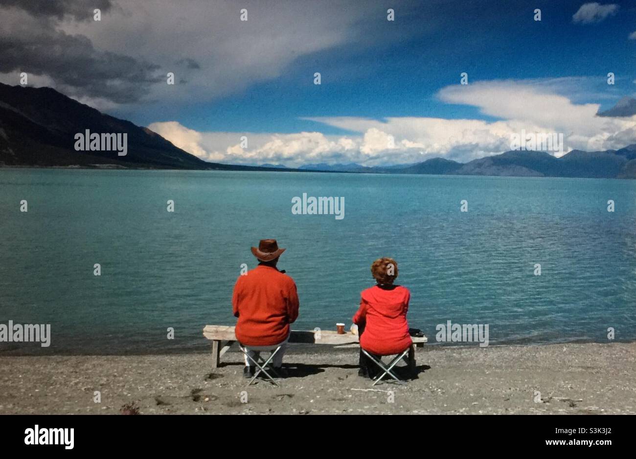 Couple having lunch sitting on  camping stools and looking out at Kluani Lake, Yukon, Canada - Smartphone Captured Stock Image