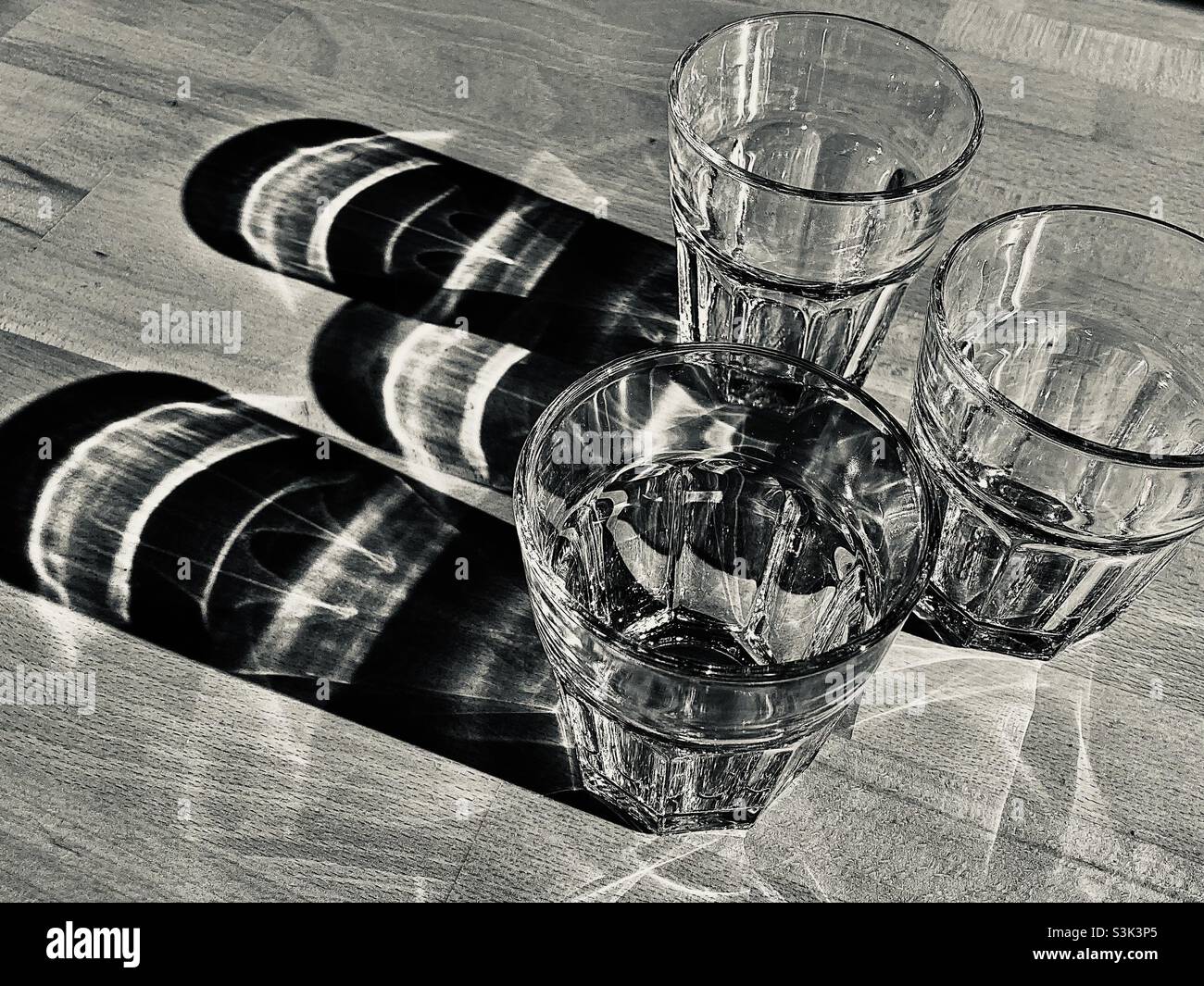 Three glass of water standing on a wooden table and casting long shadows - Smartphone Captured Stock Image