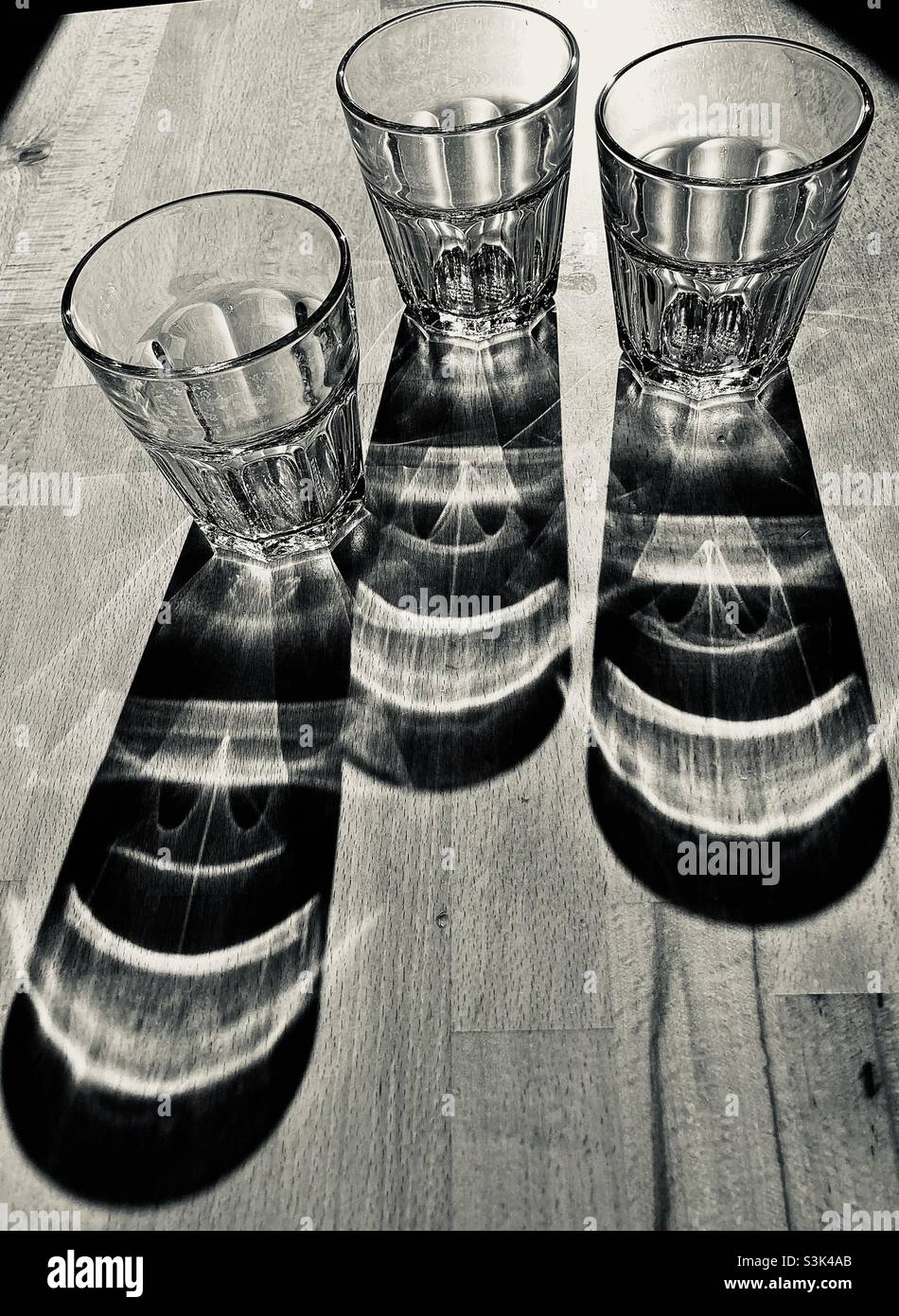 Three glass of water standing on a wooden table and casting long shadows - Smartphone Captured Stock Image