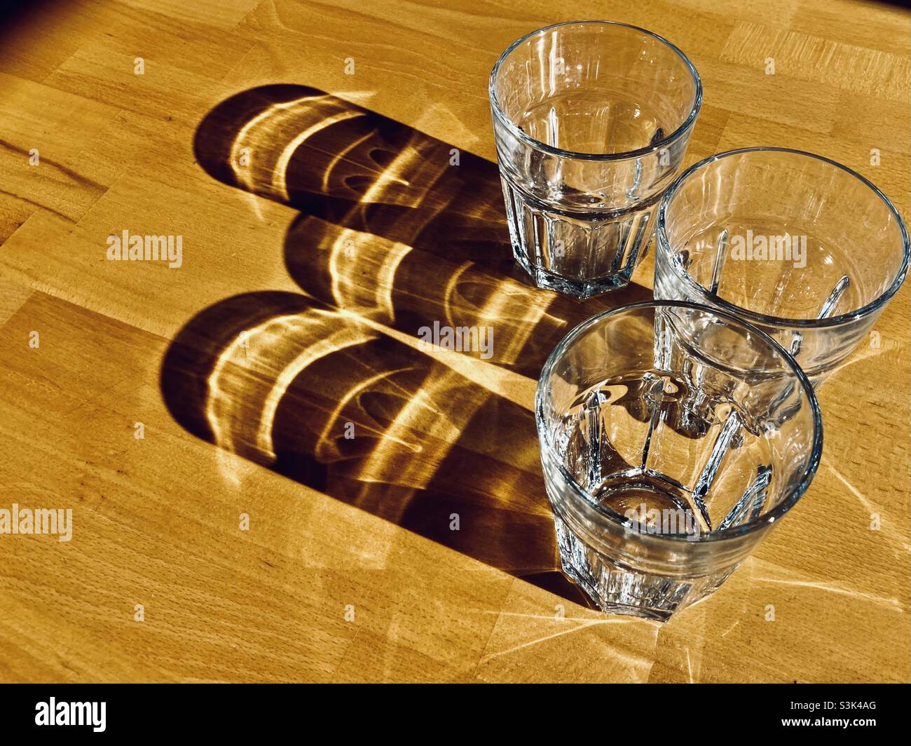 Three glass of water standing on a wooden table and casting long shadows - Smartphone Captured Stock Image