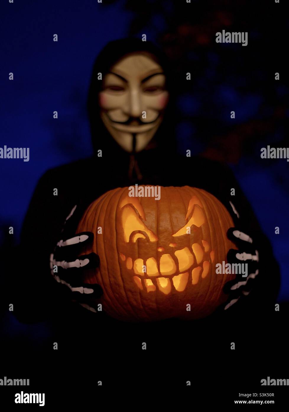 Halloween costume, Guy Fawkes mask, trick-or-treating with carved jack-o’-lantern - Smartphone Captured Stock Image