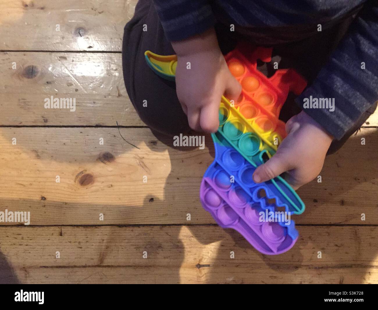 Toddler popping the blisters on a squeezable dragon. Anti-stress, pop it toy. Sensory fidget prop in a rainbow of colours. Squeezed on both sides. Quick pop-pop sounds. Stock Photo