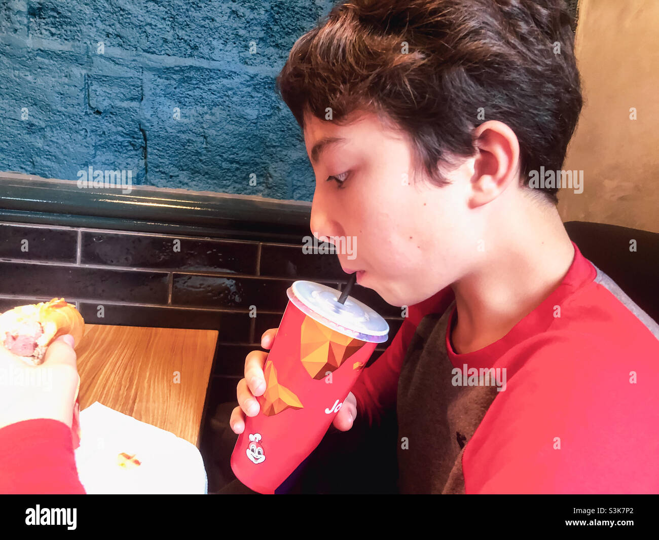 A boy drinking a soft drink in a fast food restaurant. - Smartphone Captured Stock Image