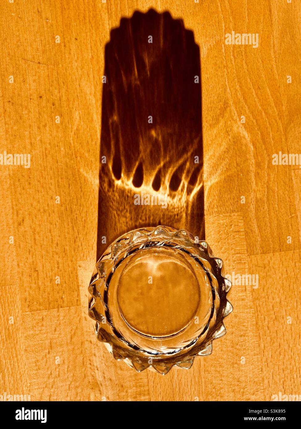 a glass of water stands on a wooden table and casts a long shadow - Smartphone Captured Stock Image