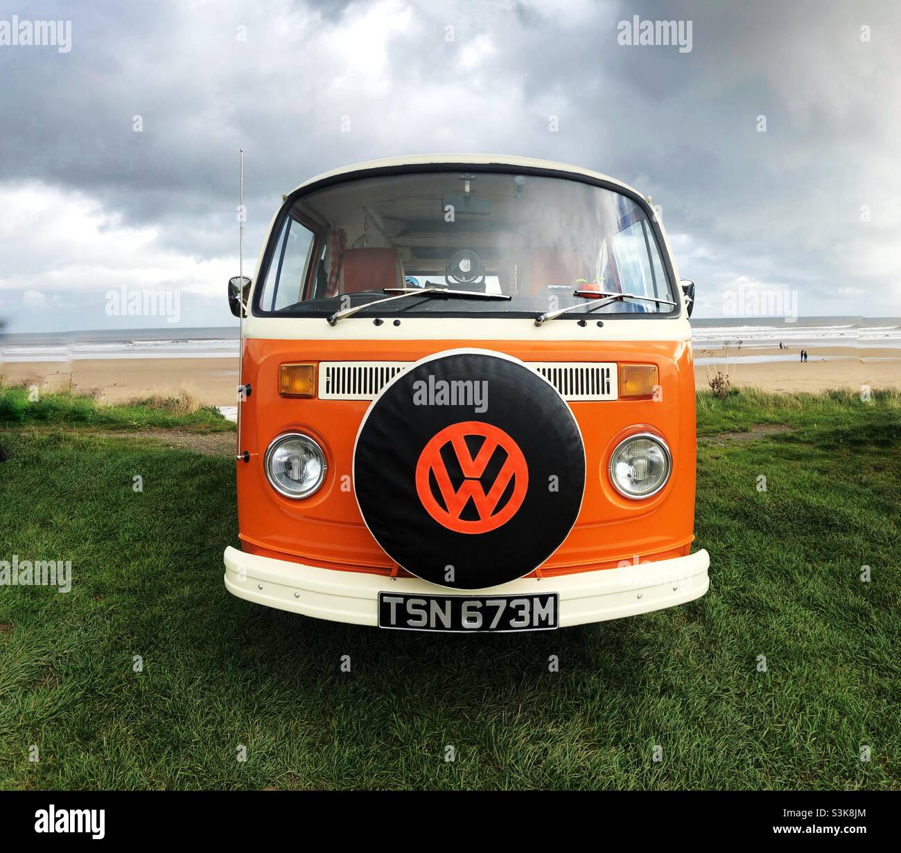 A classic VW bug campervan in orange colour with a retro feel by the beach and ocean Stock Photo