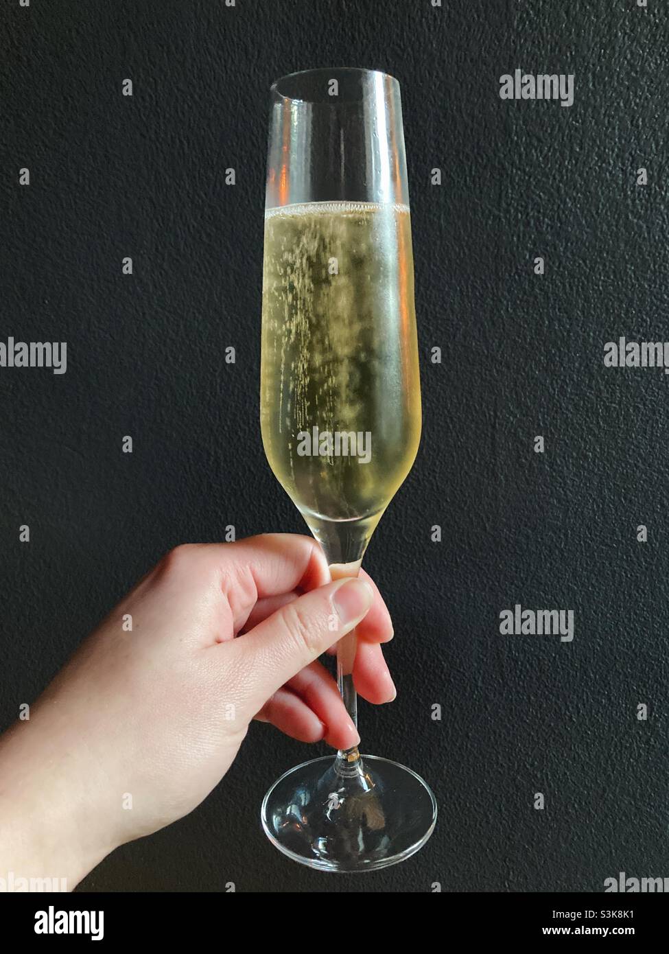 Hand holding a chilled glass of champagne with a dark grey wall behind - Smartphone Captured Stock Image