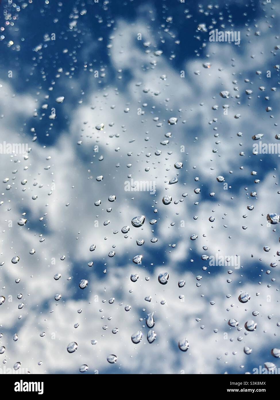Water droplets on a window with blue sky and clouds behind Stock Photo