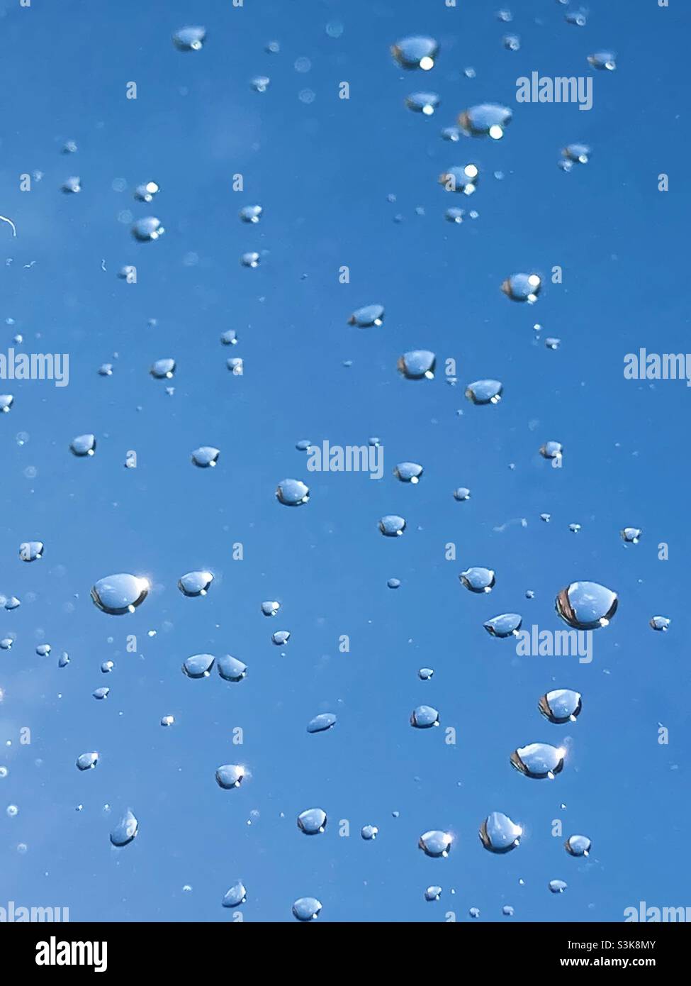 Water droplets on a window with blue sky behind Stock Photo