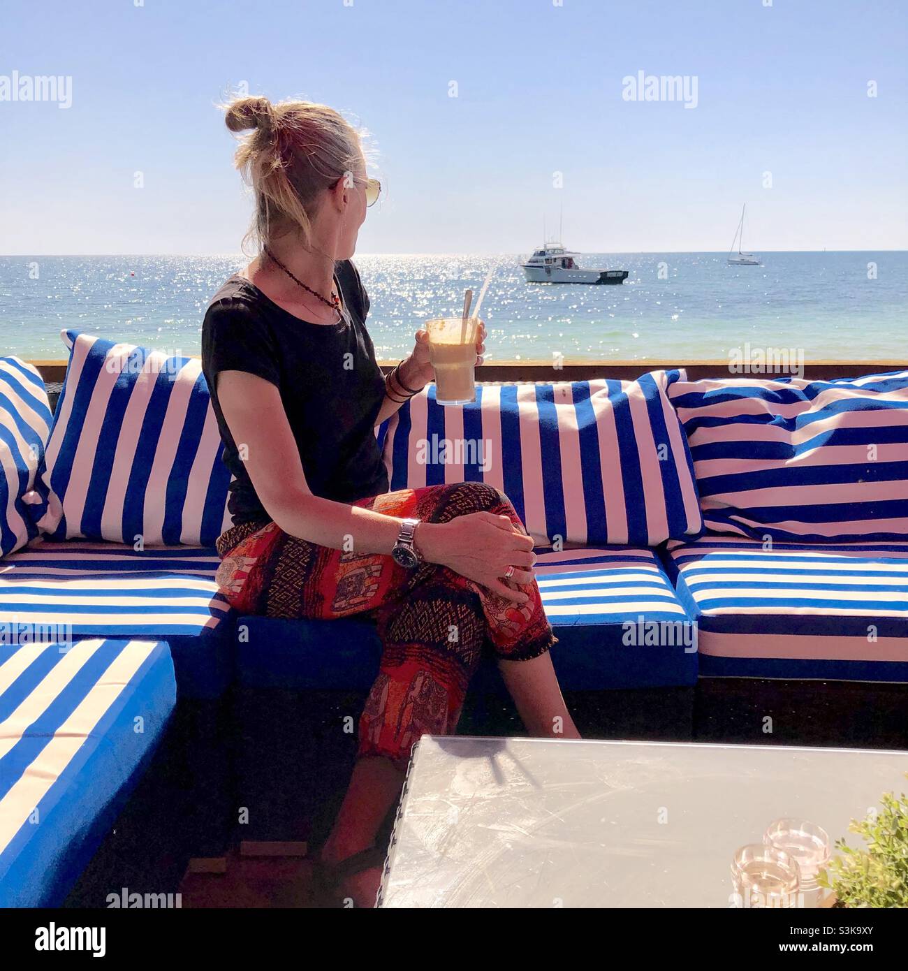 A woman with a drink enjoys the views to the ocean - Smartphone Captured Stock Image