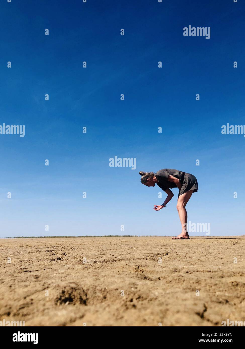 A woman picks something up from a dry desert floor - Smartphone Captured Stock Image